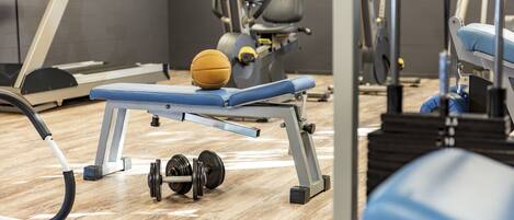 Een sportschool met trainingsapparatuur, waaronder een loopband, een hometrainer en gewichten.