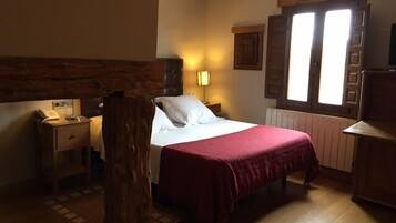 Ein Schlafzimmer mit Holz-Kopfteil, einem Bett mit roter Bettdecke, einem Nachttisch mit Lampe und einem Fenster mit Holzjalousien.