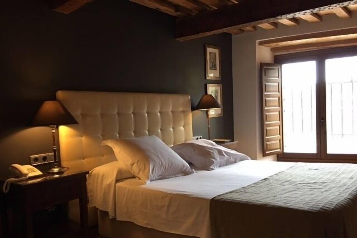 Un dormitorio con una cama grande, dos lámparas de noche, una mesita de noche y una ventana con persianas.
