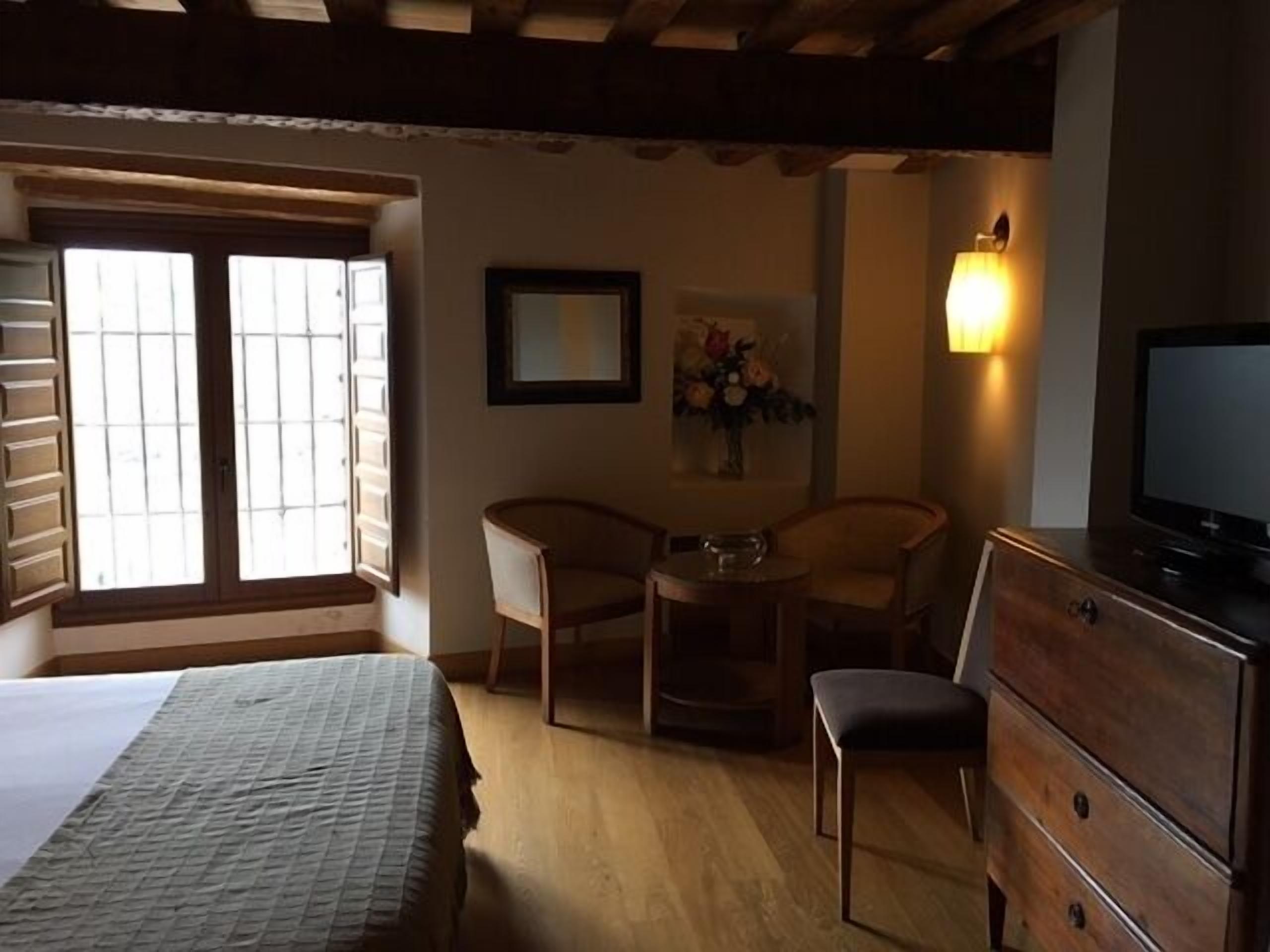 Un dormitorio con cama, escritorio, dos sillas, cómoda, televisor y ventana con persianas.
