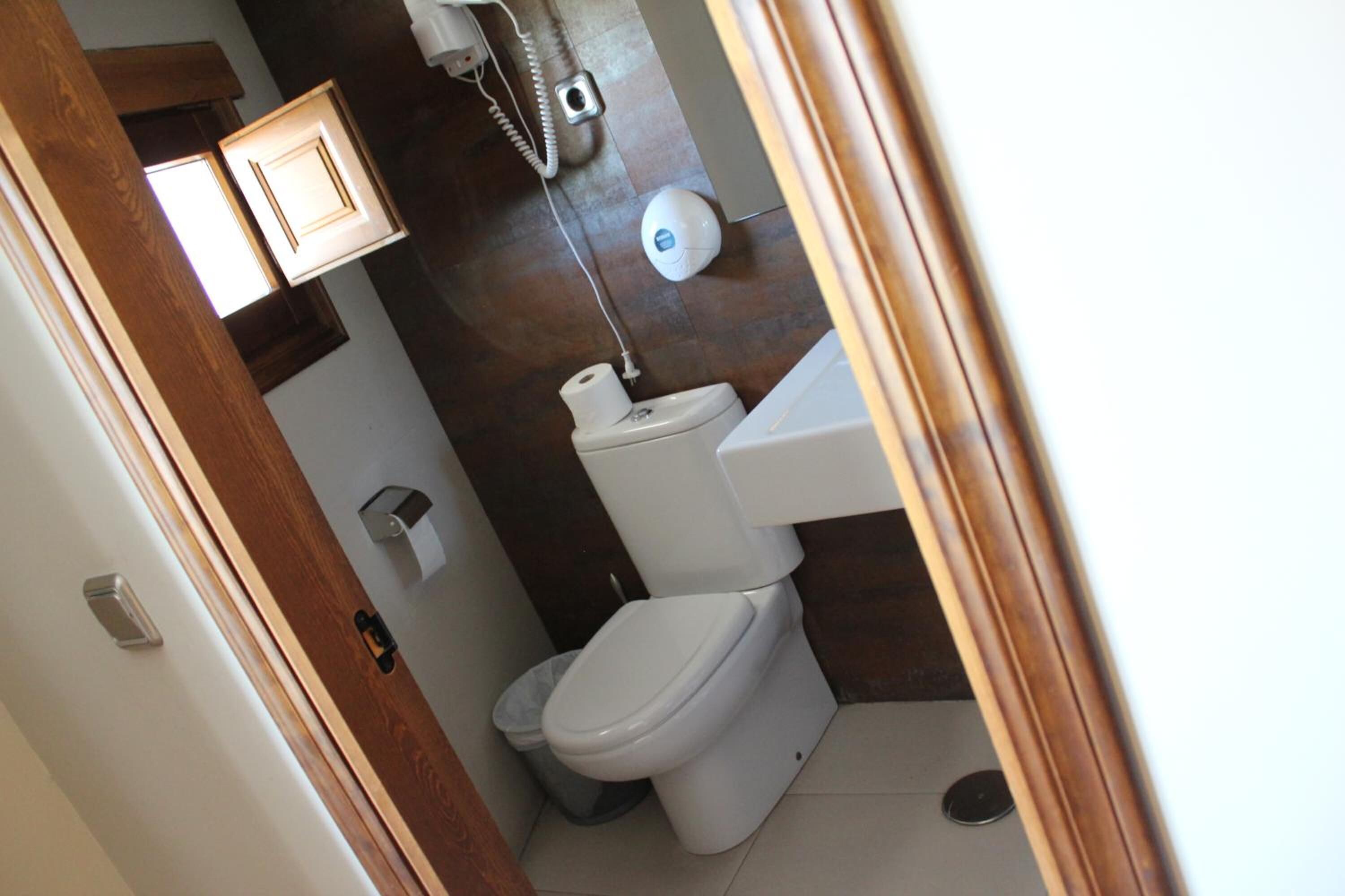 A compact bathroom with a toilet, a hand dryer, and a small trash bin.