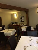 Comedor con mesas dispuestas para dos, con manteles blancos y vajilla sencilla.