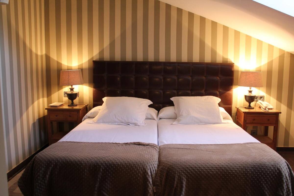 Una cama doble con cabecera oscura, dos mesitas de noche con lámparas y papel tapiz a rayas.