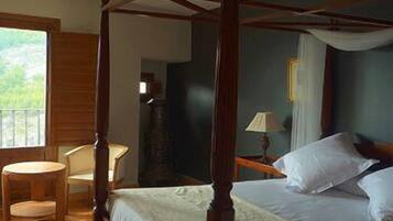 Un letto a baldacchino con tenda, un tavolo rotondo in legno e una sedia in una stanza con vista su un balcone.