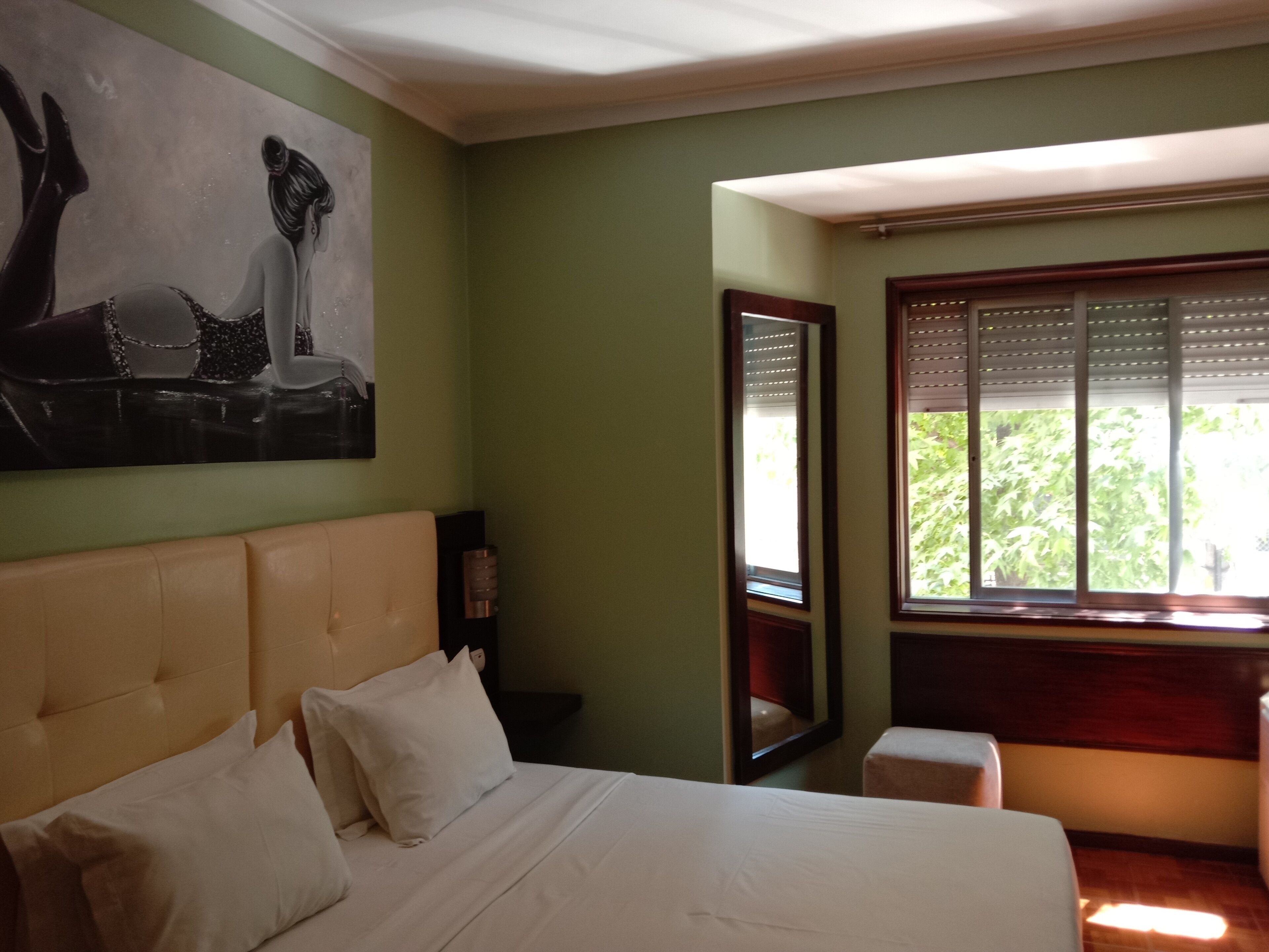 Ein Schlafzimmer mit einem großen Bett, einem Nachttisch, einem Spiegel und einem Fenster mit Jalousien.