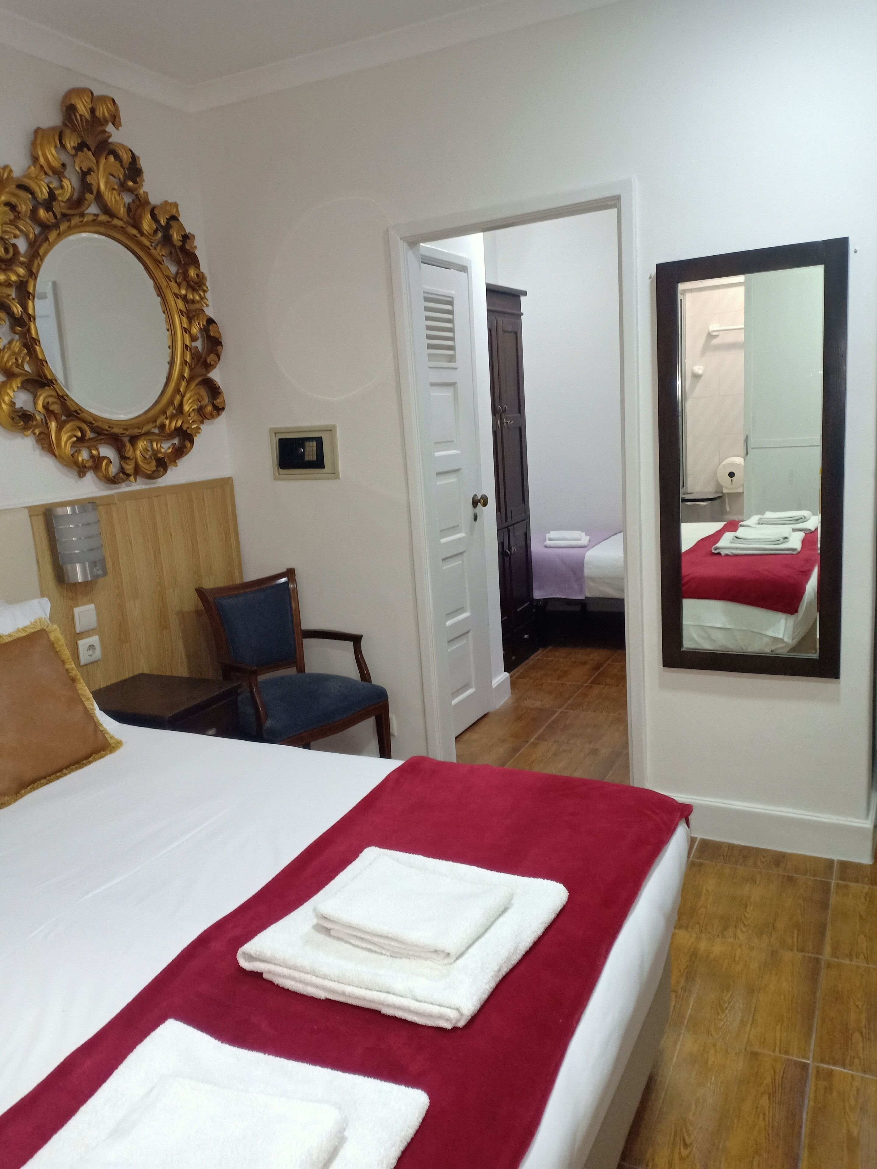 A hotel room with a bed, a desk, a chair, a wardrobe, and a bathroom visible through an open door.