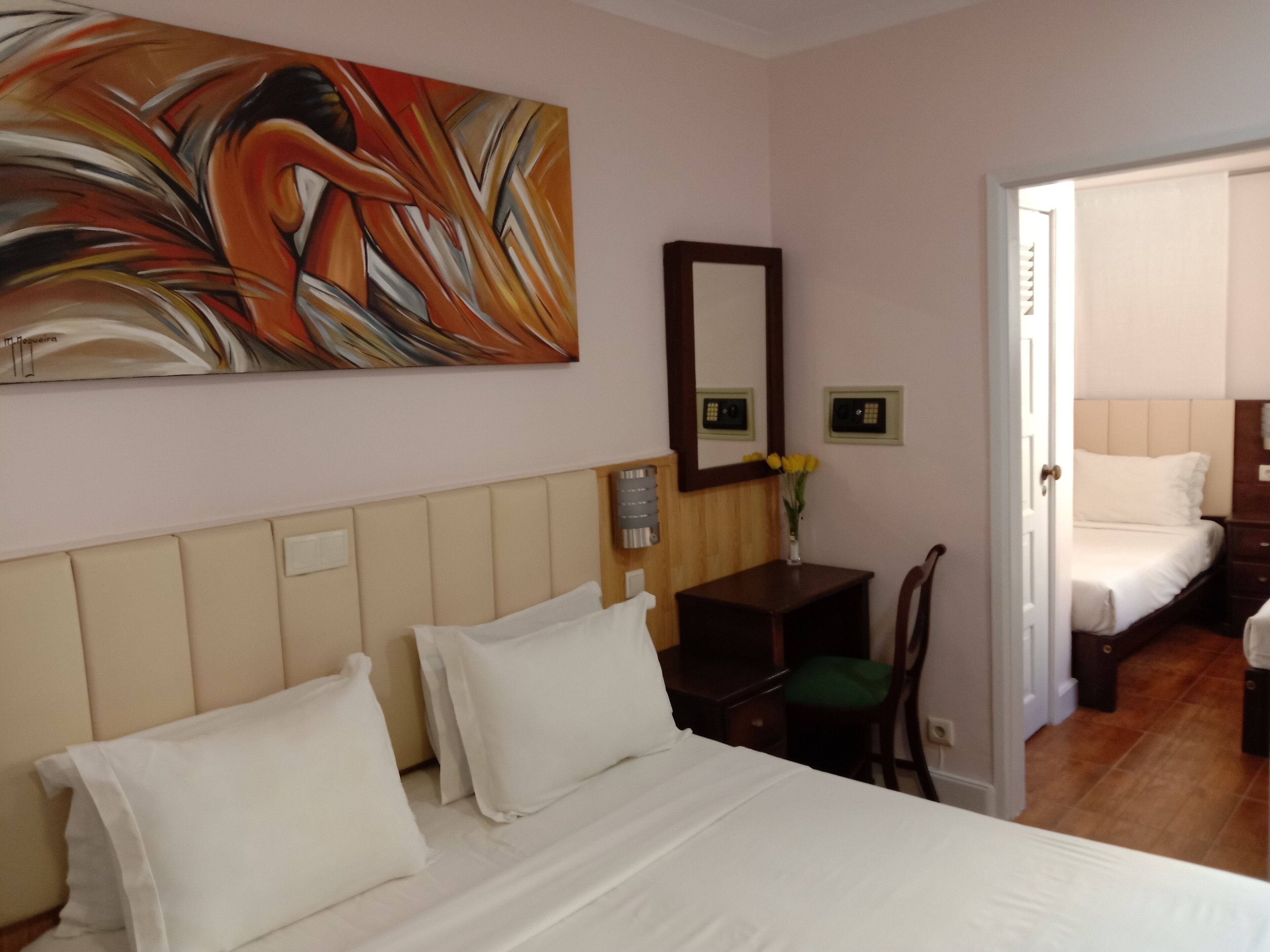 Una camera d'albergo con un letto, una scrivania, una sedia, uno specchio e un quadro appeso al muro.