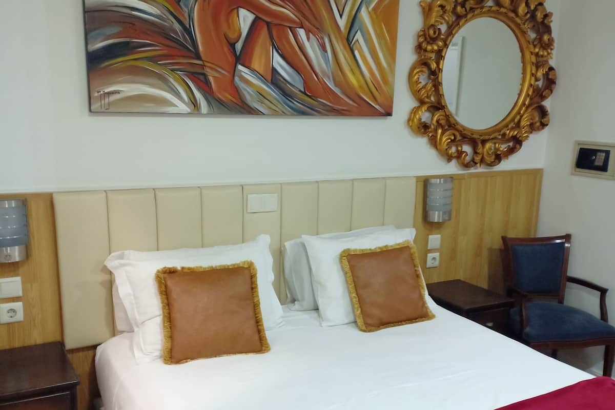 A hotel room with a large bed, a red throw blanket, white pillows, and a colorful abstract painting above the bed.
