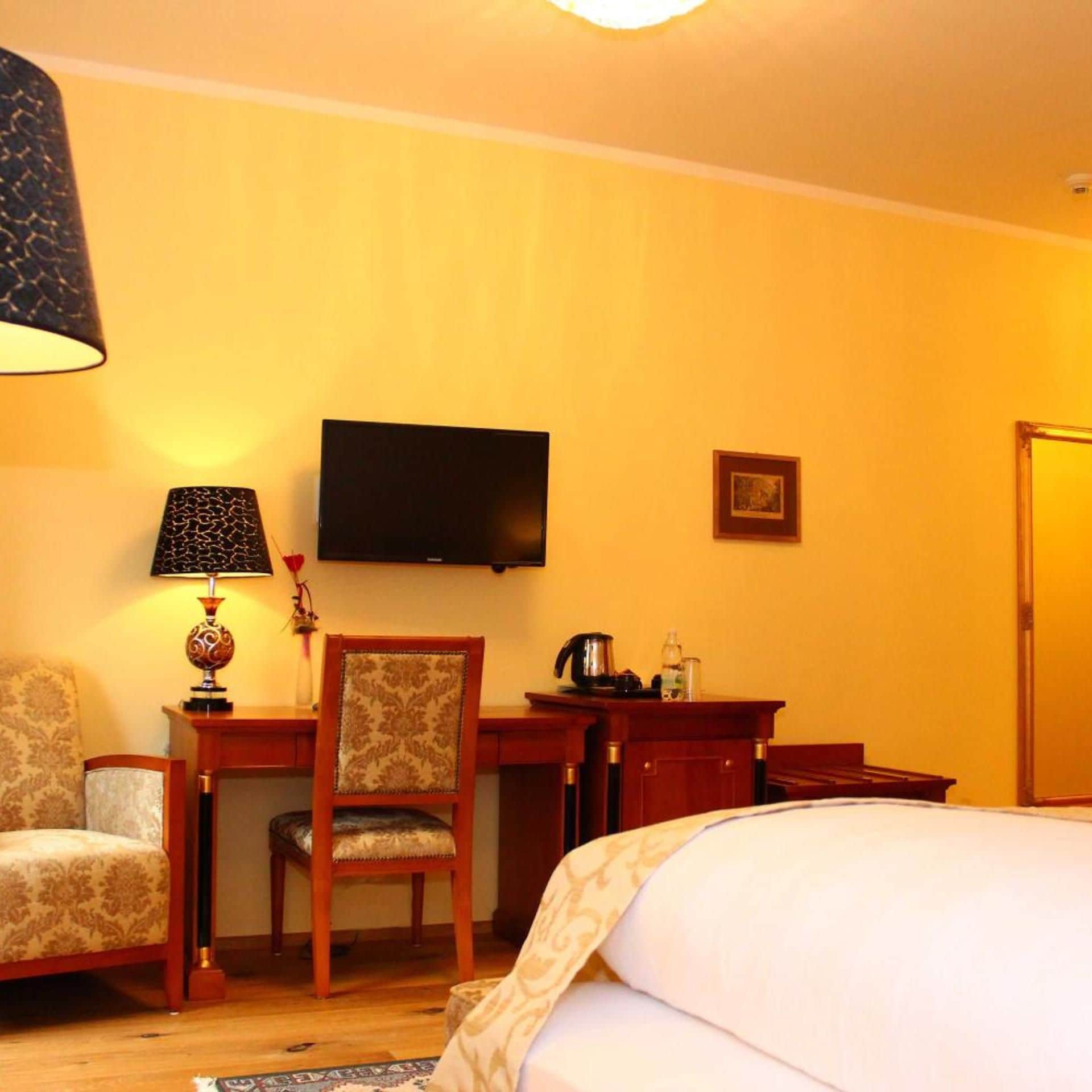 Habitación de hotel con una cama, un escritorio con silla, un televisor y una mesita de noche con lámpara.