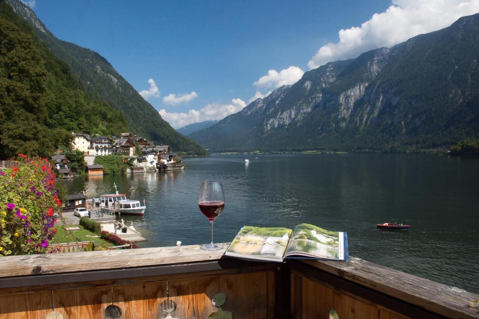 A lakeside view with a wooden deck, a glass of red wine, and a book.