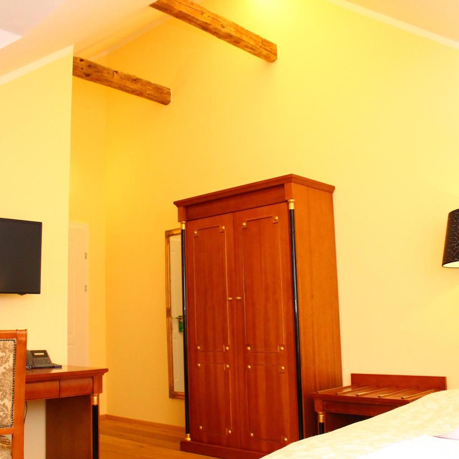A room with a wooden wardrobe, a desk, a bed, and a television mounted on the wall.