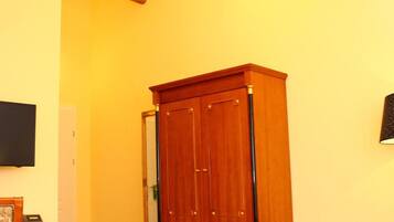 A room with a wooden wardrobe, a desk, a bed, and a television mounted on the wall.