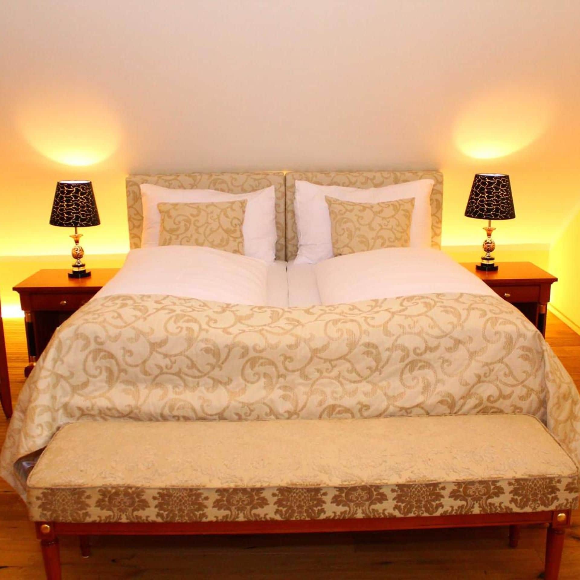 A double bed with a patterned bedspread and two bedside lamps.
