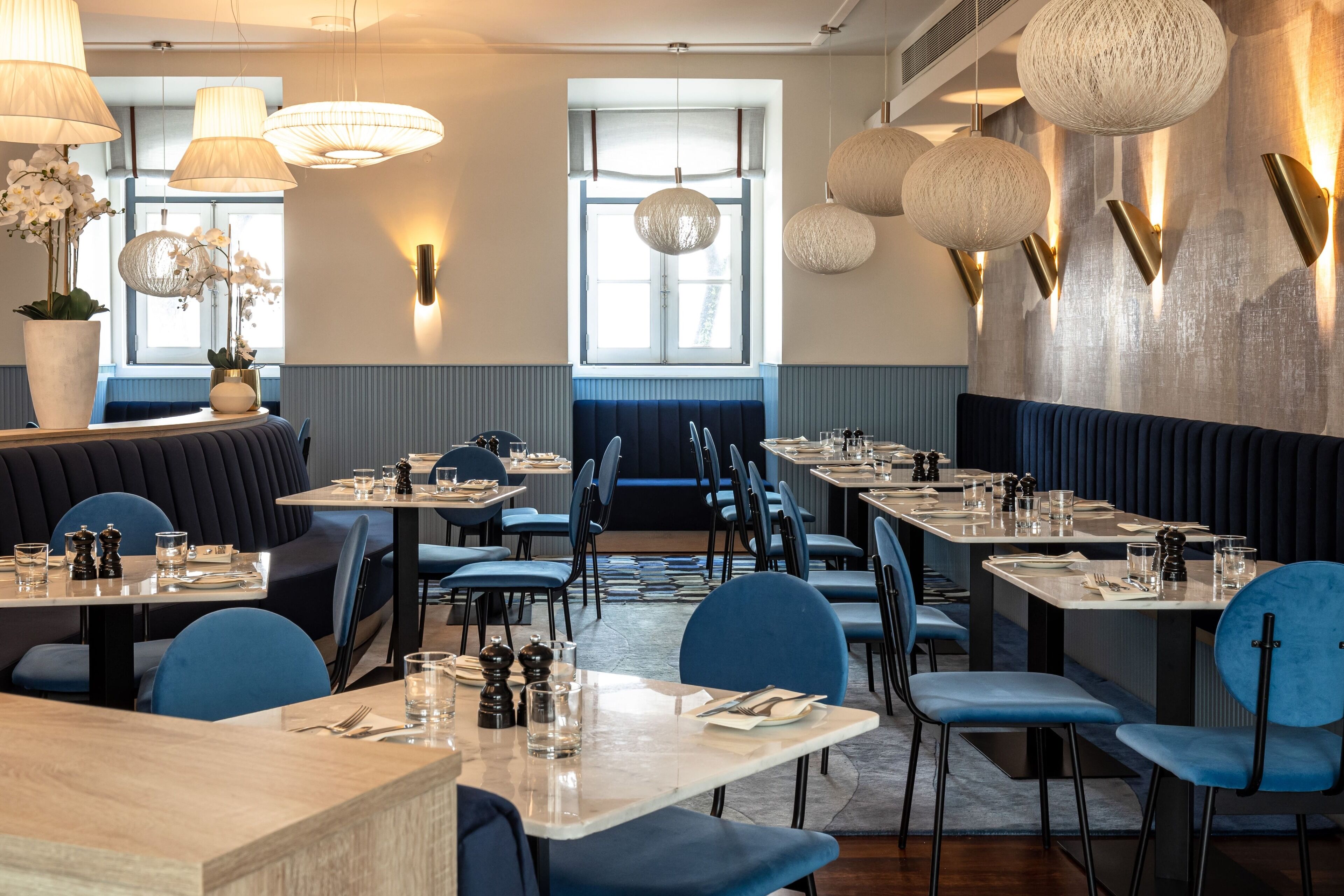 Un restaurante con asientos tipo banca y mesas, iluminación colgante moderna y vistas al exterior a través de amplias ventanas.