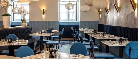 Un restaurante con asientos tipo banca y mesas, iluminación colgante moderna y vistas al exterior a través de amplias ventanas.