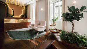 Un interior moderno con un mostrador de recepción de madera, un sillón cómodo, una alfombra verde y una planta grande.