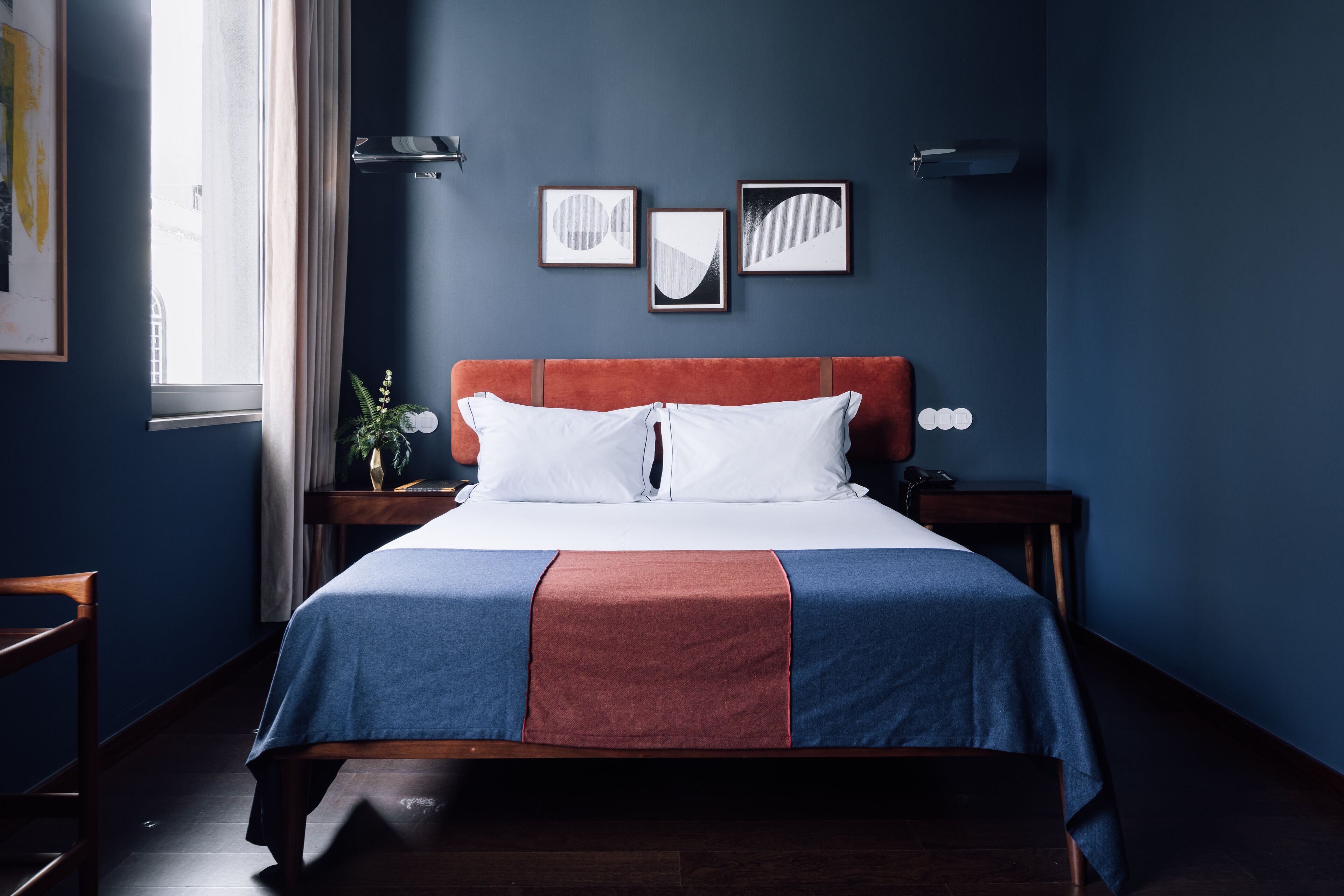 Un dormitorio con una cama, una mesita de noche, una lámpara y cuadros en la pared.