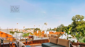 Una terraza en la azotea con mobiliario exterior, incluyendo sofás y sillones, y vistas a la ciudad de fondo.