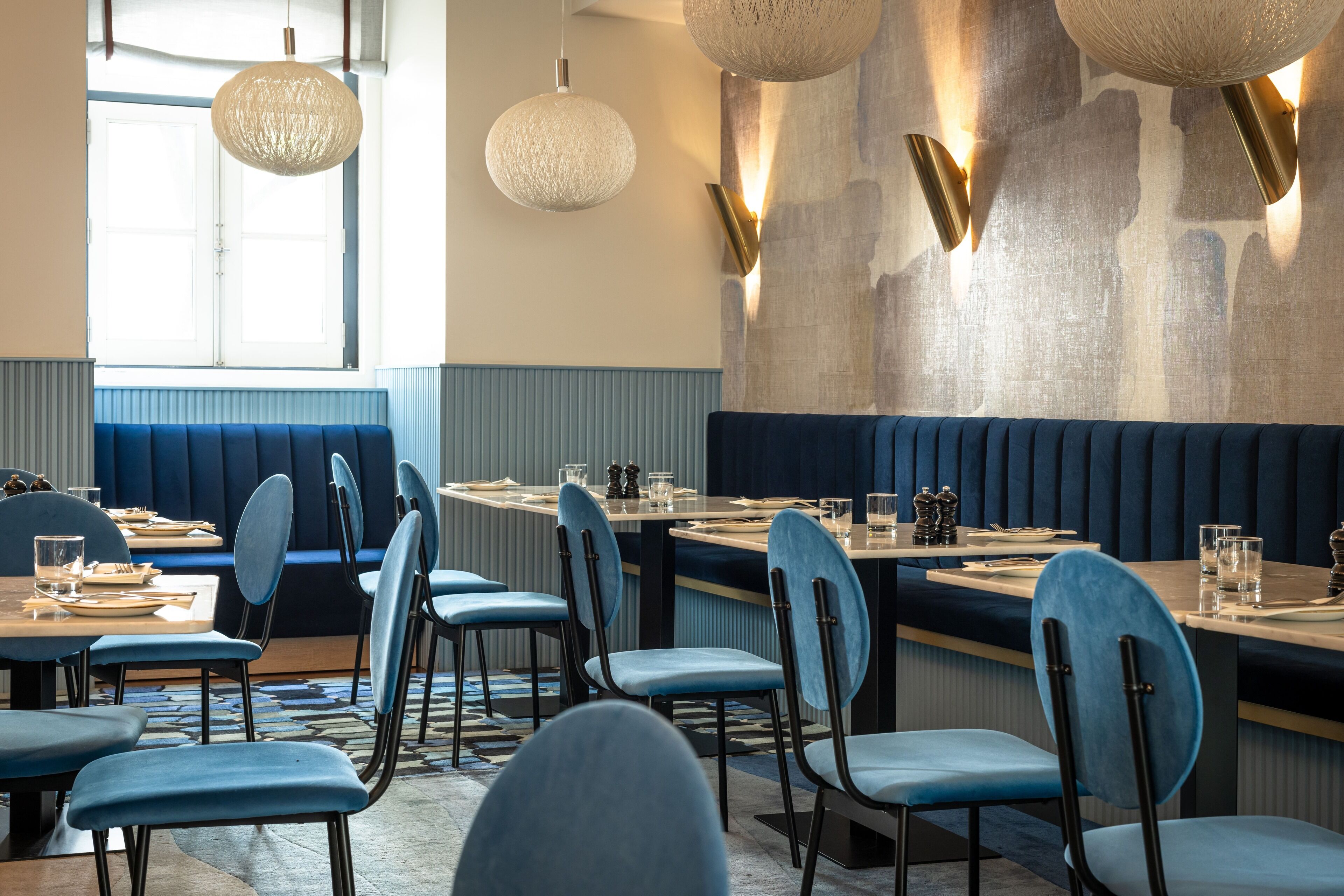 Un restaurante con asientos tapizados en azul, mesas redondas e iluminación colgante.