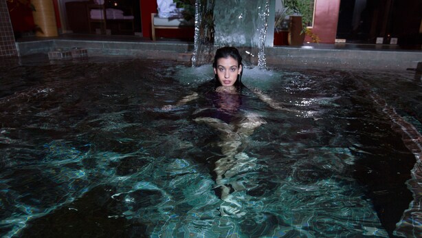 Una persona en una piscina con agua cristalina, rodeada de un suelo de azulejos y una pared roja.