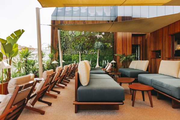 A modern outdoor seating area with wooden furniture and a green sofa, surrounded by plants and a wooden wall.