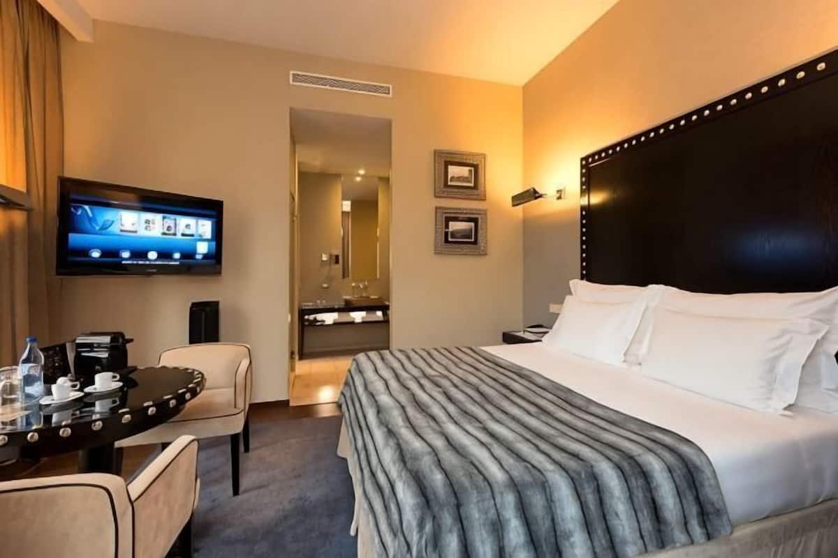 A hotel room with a bed, a TV, a desk, and a chair.