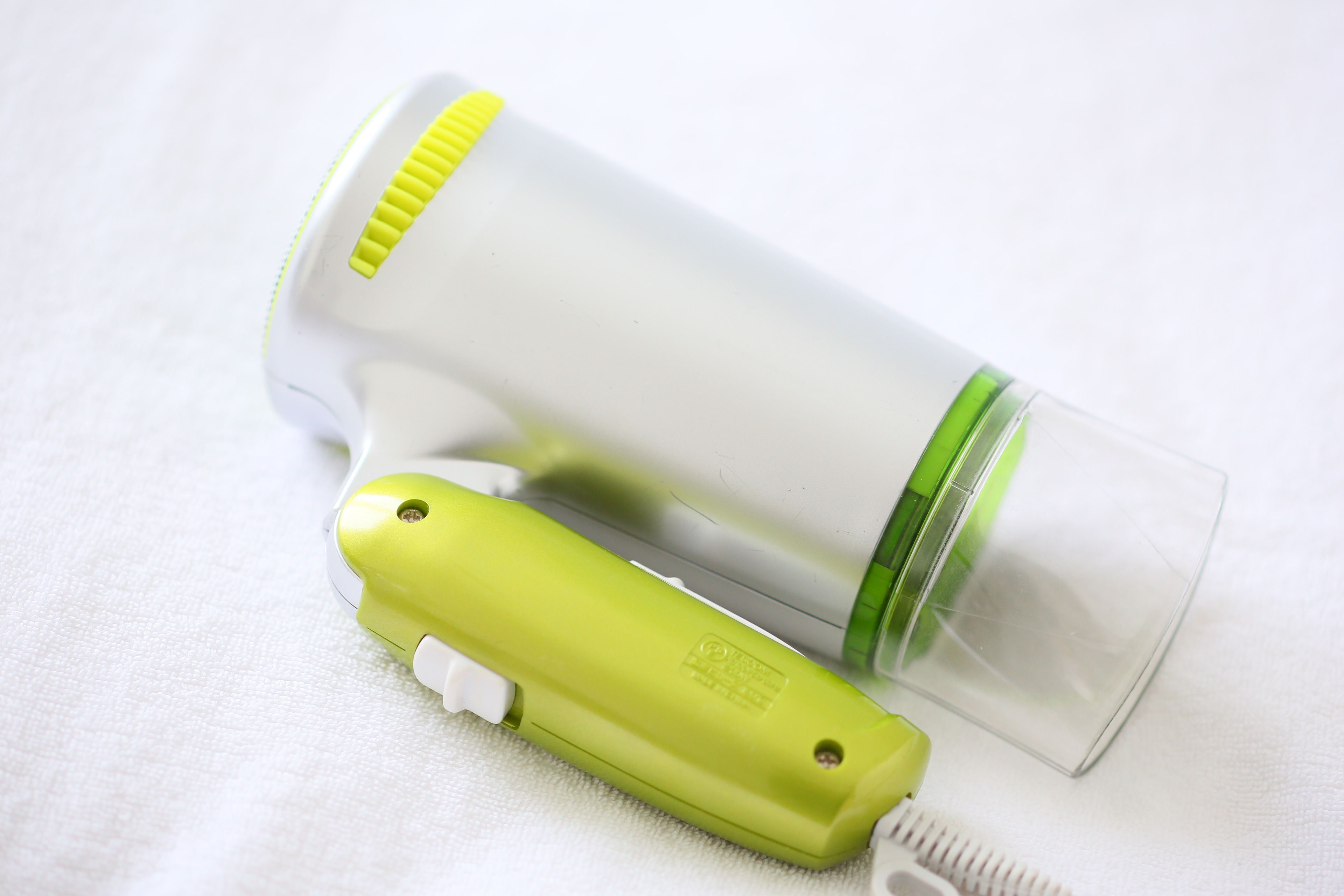 A compact, portable device with a green and white color scheme, likely a personal hygiene item, placed on a white fabric surface.