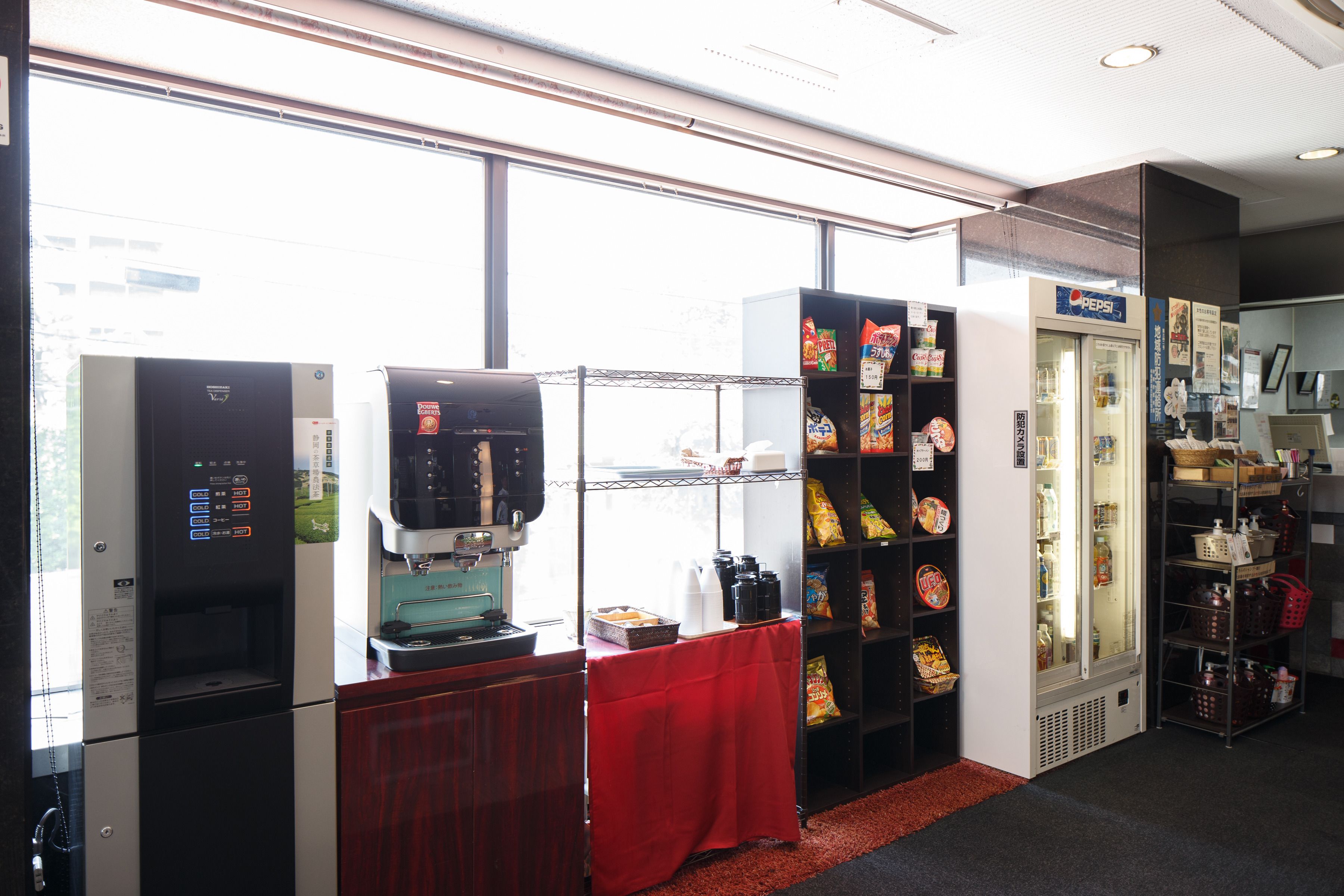 A vending area with a refrigerator, coffee machine, and shelves stocked with snacks.
