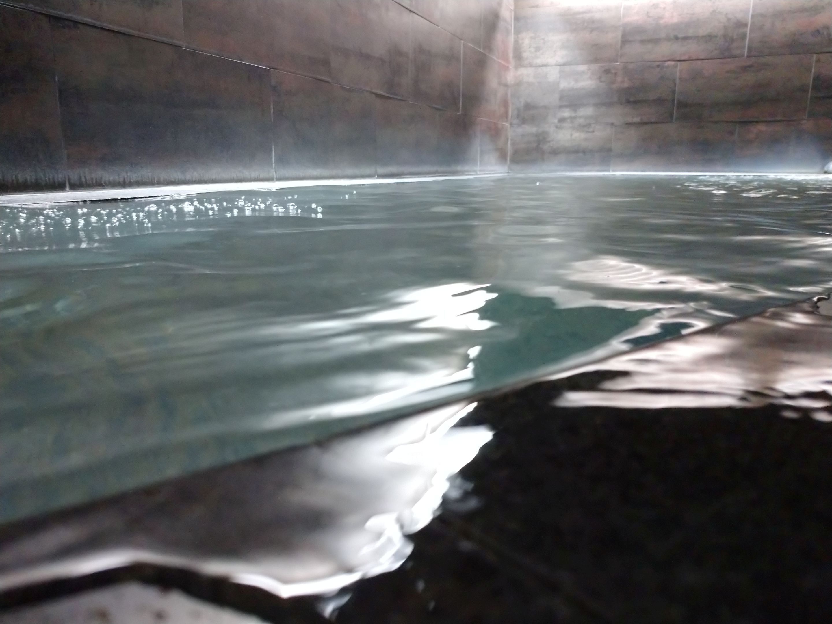 Uma grande piscina interior com água cristalina, ladeada por paredes de pedra.