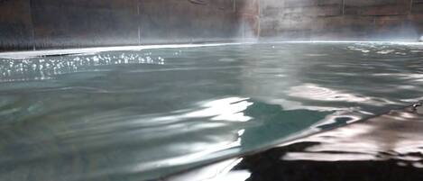 Uma grande piscina interior com água cristalina, ladeada por paredes de pedra.