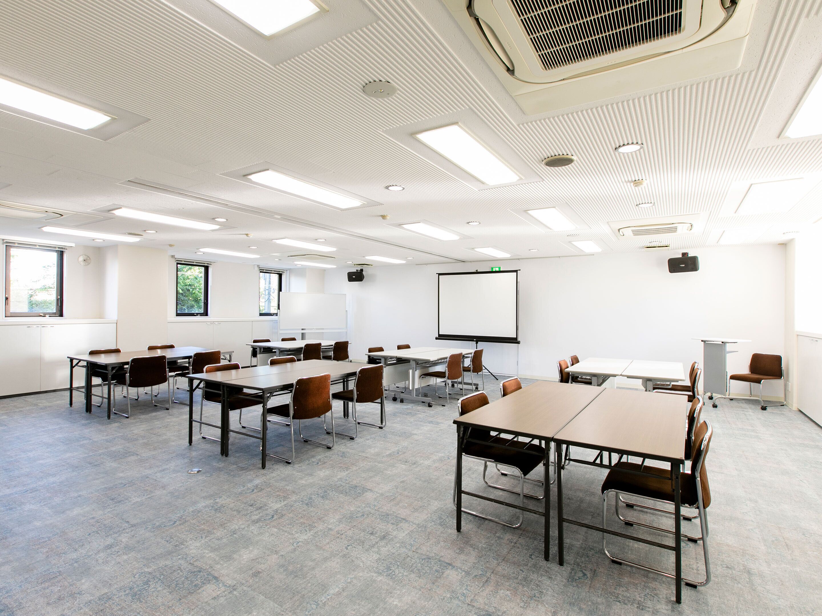 A conference room with multiple tables and chairs, a whiteboard, and a projector screen.