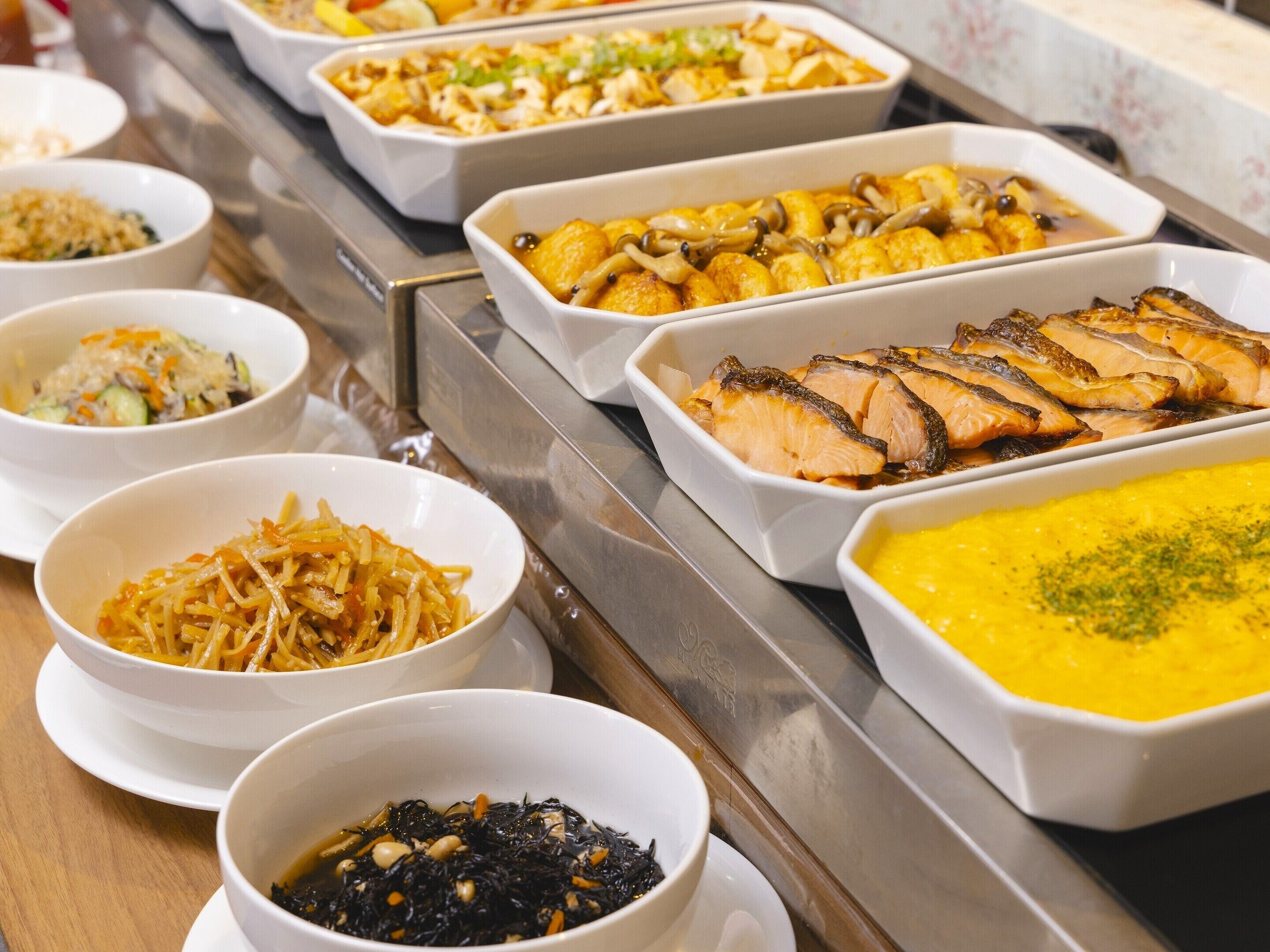 Buffet amb diversos plats, com ara salmó, fideus i una sopa groga.
