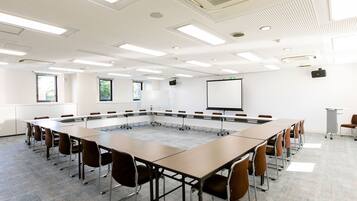 Uma sala de conferências com uma grande mesa oval, várias cadeiras, uma tela de projetor e um quadro branco.