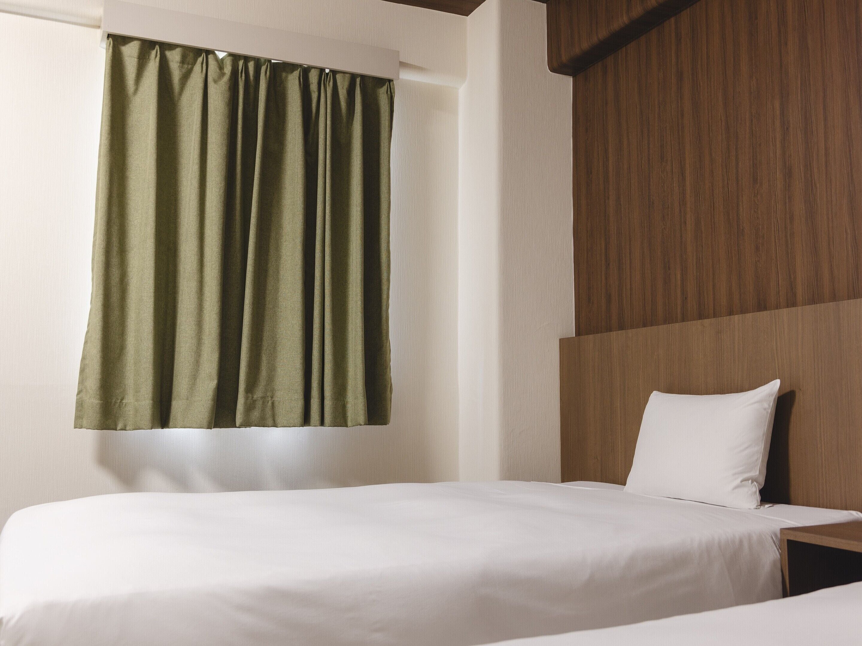 A hotel room with a bed, a pillow, and a window with a green curtain.