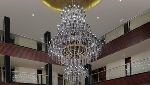 A multi-level hotel lobby with a grand chandelier, a central seating area with a flower arrangement, and a circular seating arrangement on the lower level. - Royalton Hyderabad (Hyderabad)
