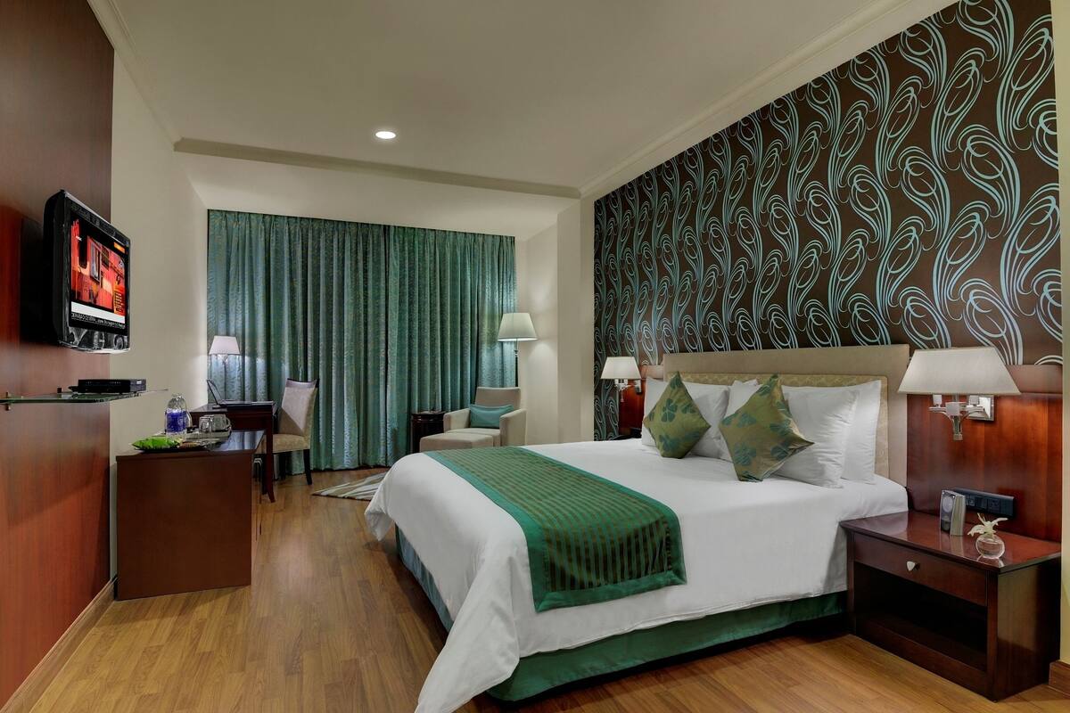 Quarto de hotel com uma cama grande, uma escrivaninha, uma televisão e parede estampada.