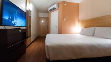 Hotellihuone, jossa on sänky, televisio, vaatekaappi ja ilmastointilaite.