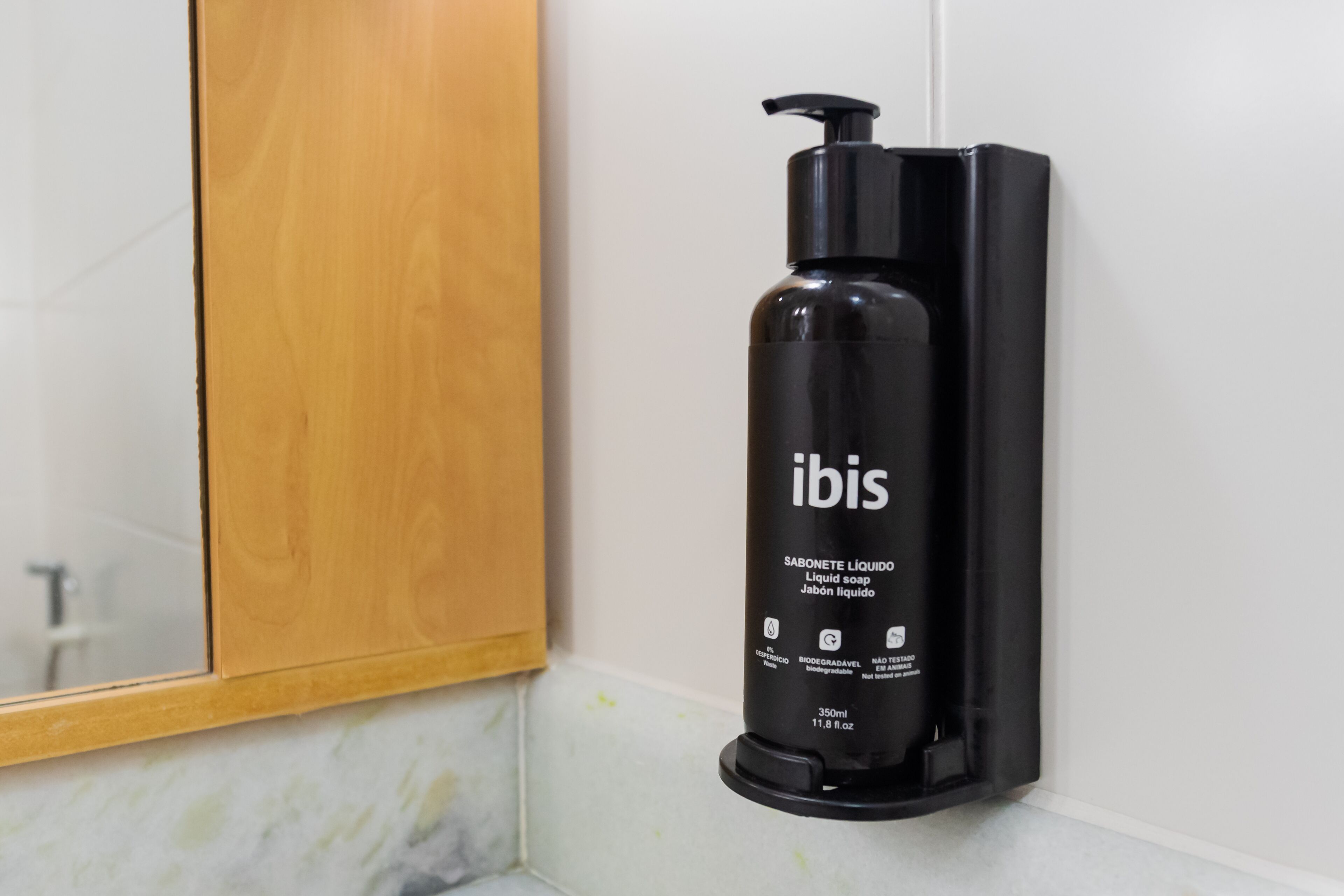 A black bottle of liquid soap labeled 'ibis' mounted on a white wall.