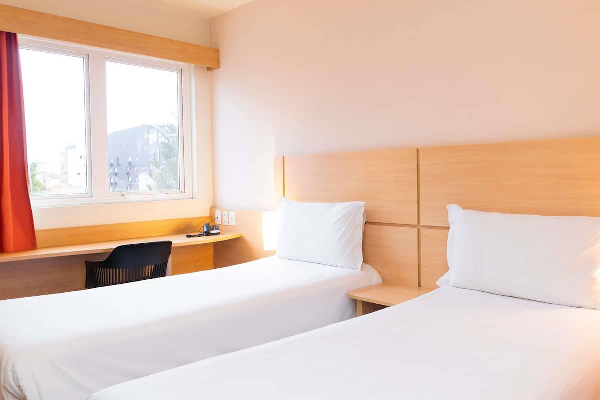 Une chambre d’hôtel avec deux lits, un bureau, une chaise et une fenêtre avec des rideaux.