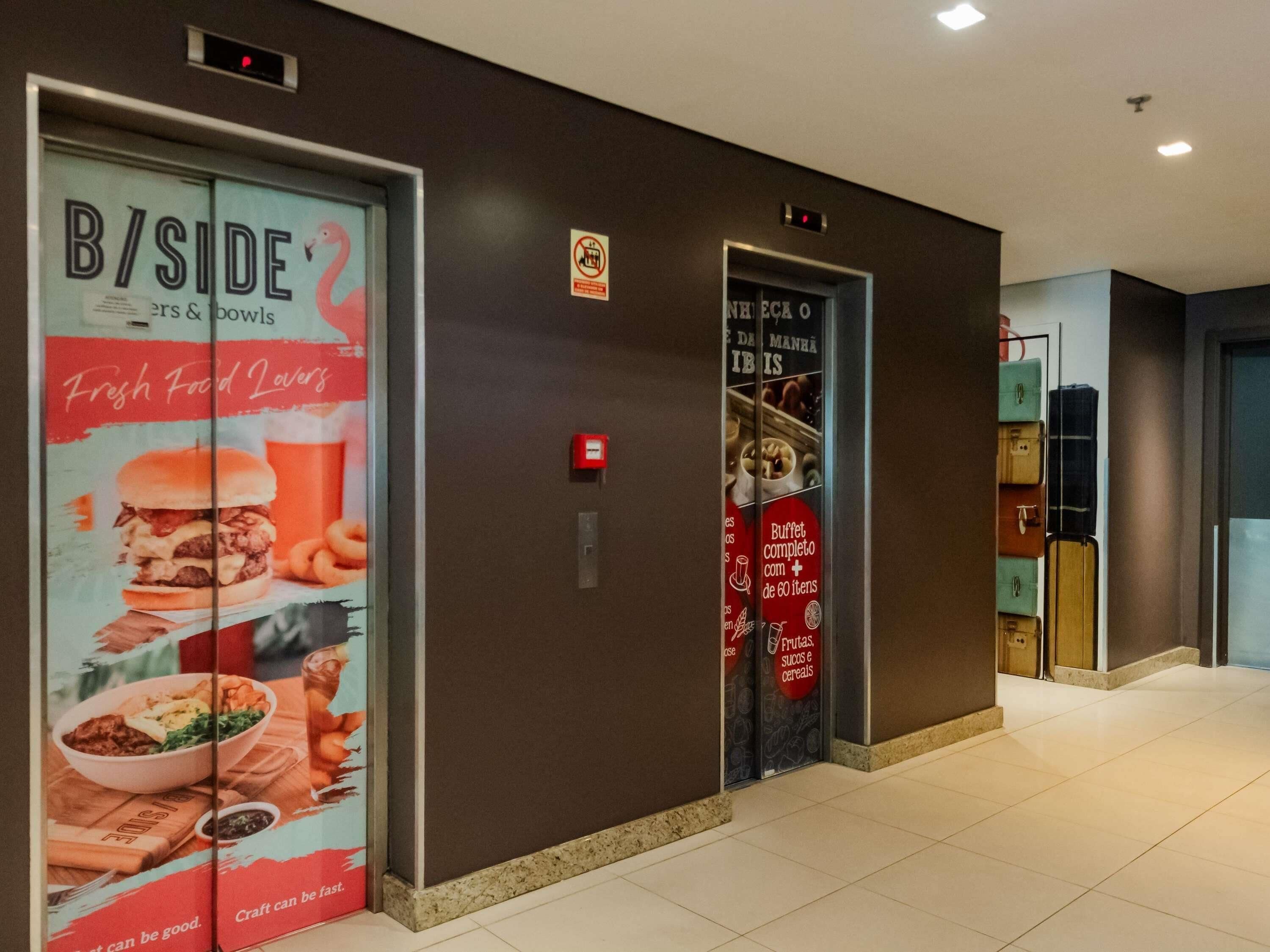 Un pasillo con un ascensor, un anuncio de restaurante en la pared y un portaequipajes.