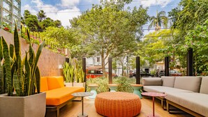 A modern outdoor seating area with a sofa, ottoman, and tables, surrounded by potted plants and a view of the city. - ibis Porto Alegre Moinhos de Vento (Porto Alegre)