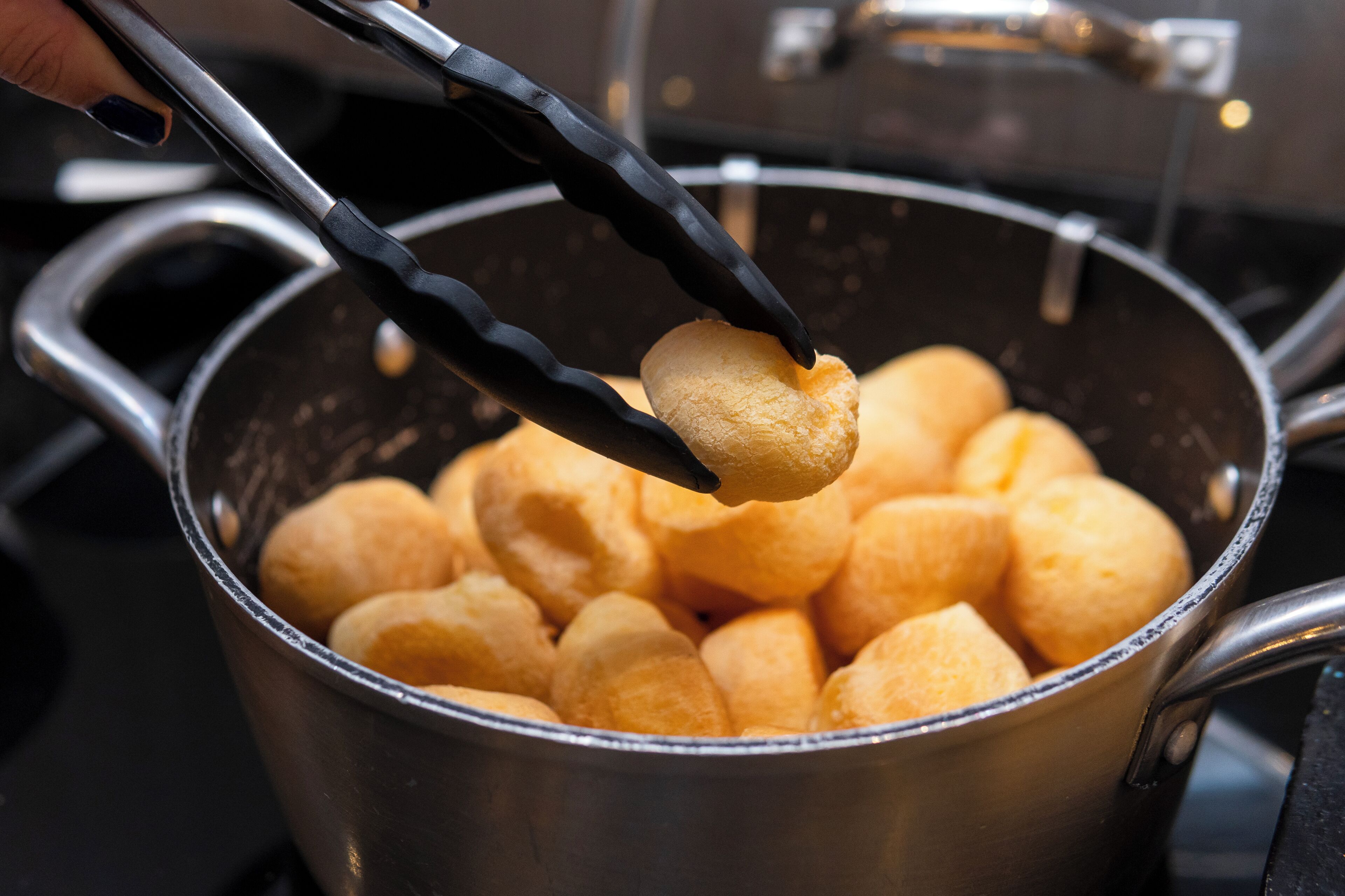 A pot filled with golden-brown bread rolls being held by tongs.