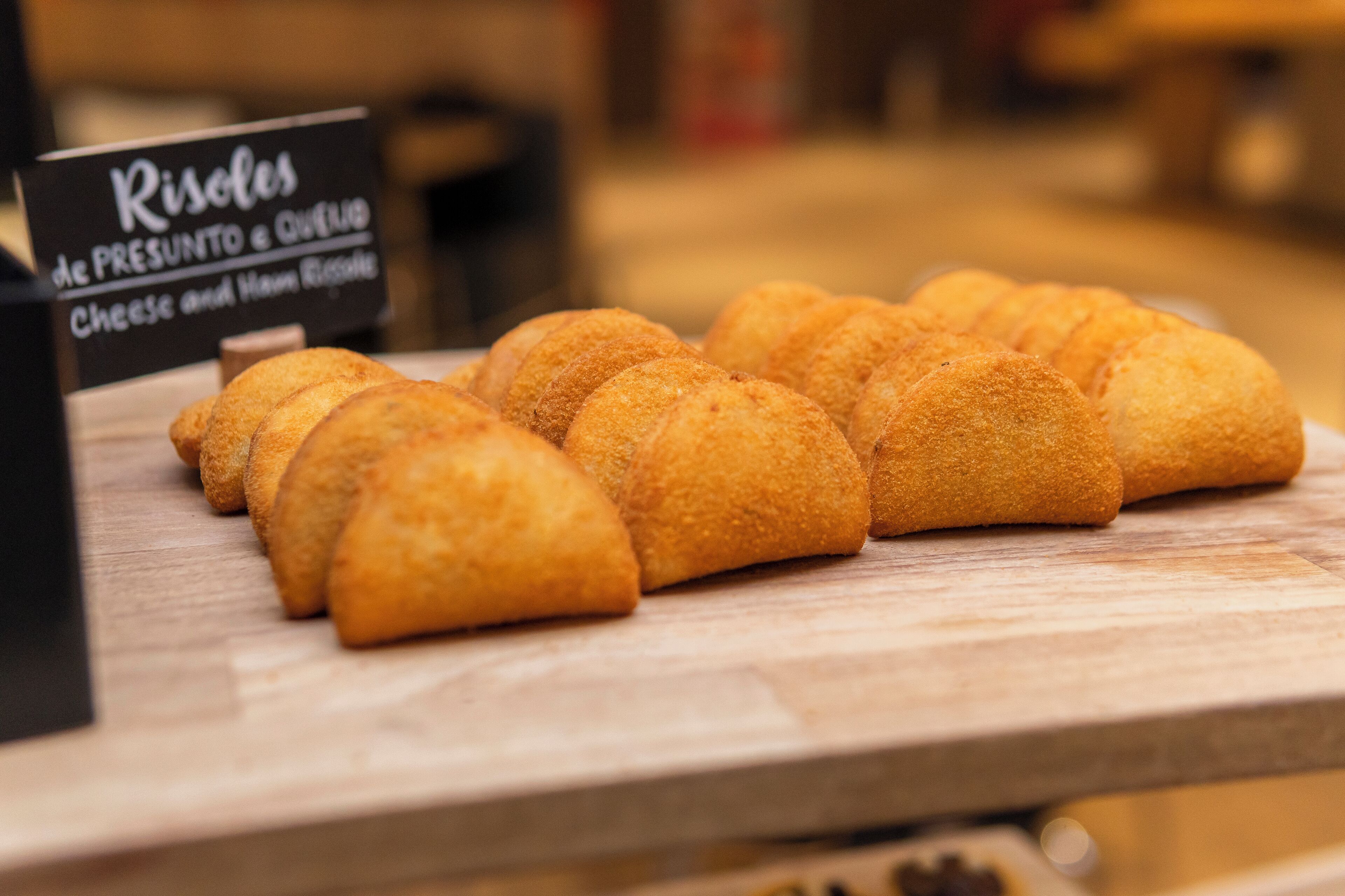 Une variété de viennoiseries dorées et brunes est exposée sur une surface en bois, et une pancarte indique qu’il s’agit de roulés au fromage et au jambon.