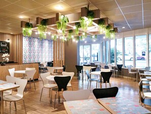 Interior de restaurante con plantas colgantes, piso de madera y ventanas amplias.