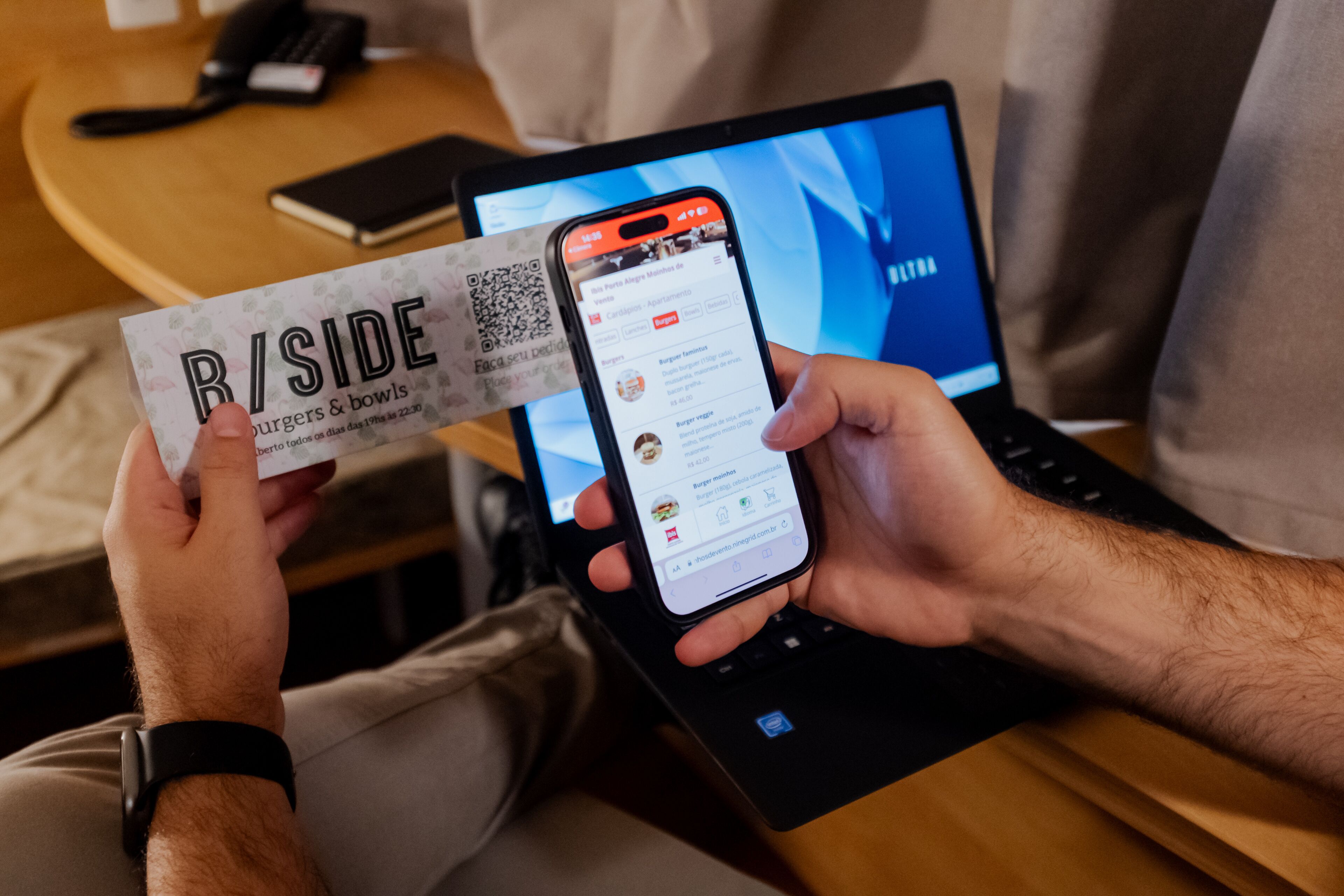 A person holding a smartphone and a business card with the text "B/SIDE burgers & bowls" and a QR code.