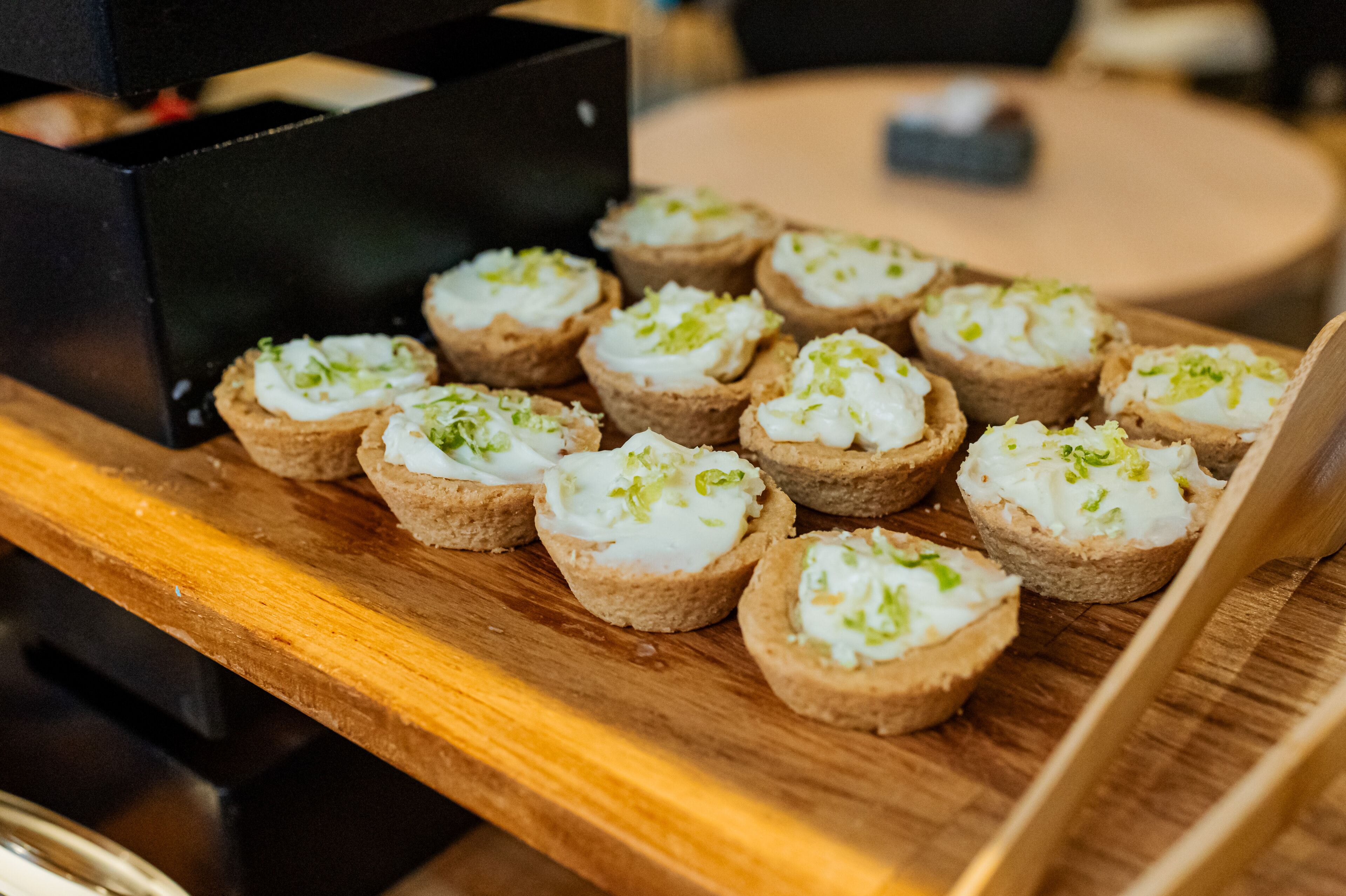 A wooden table with several small pastries topped with cream and green garnish.