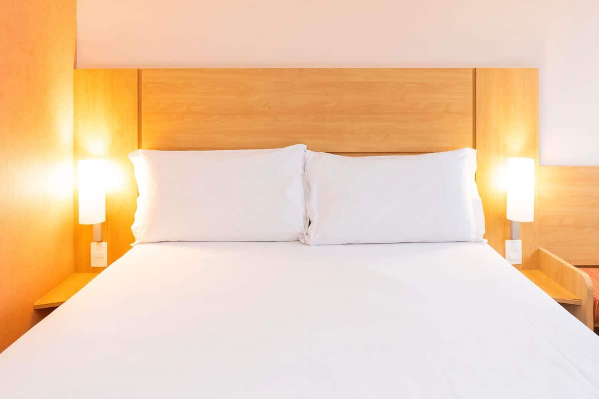 Un lit bien fait, avec du linge de lit blanc et deux lampes de chevet de chaque côté.