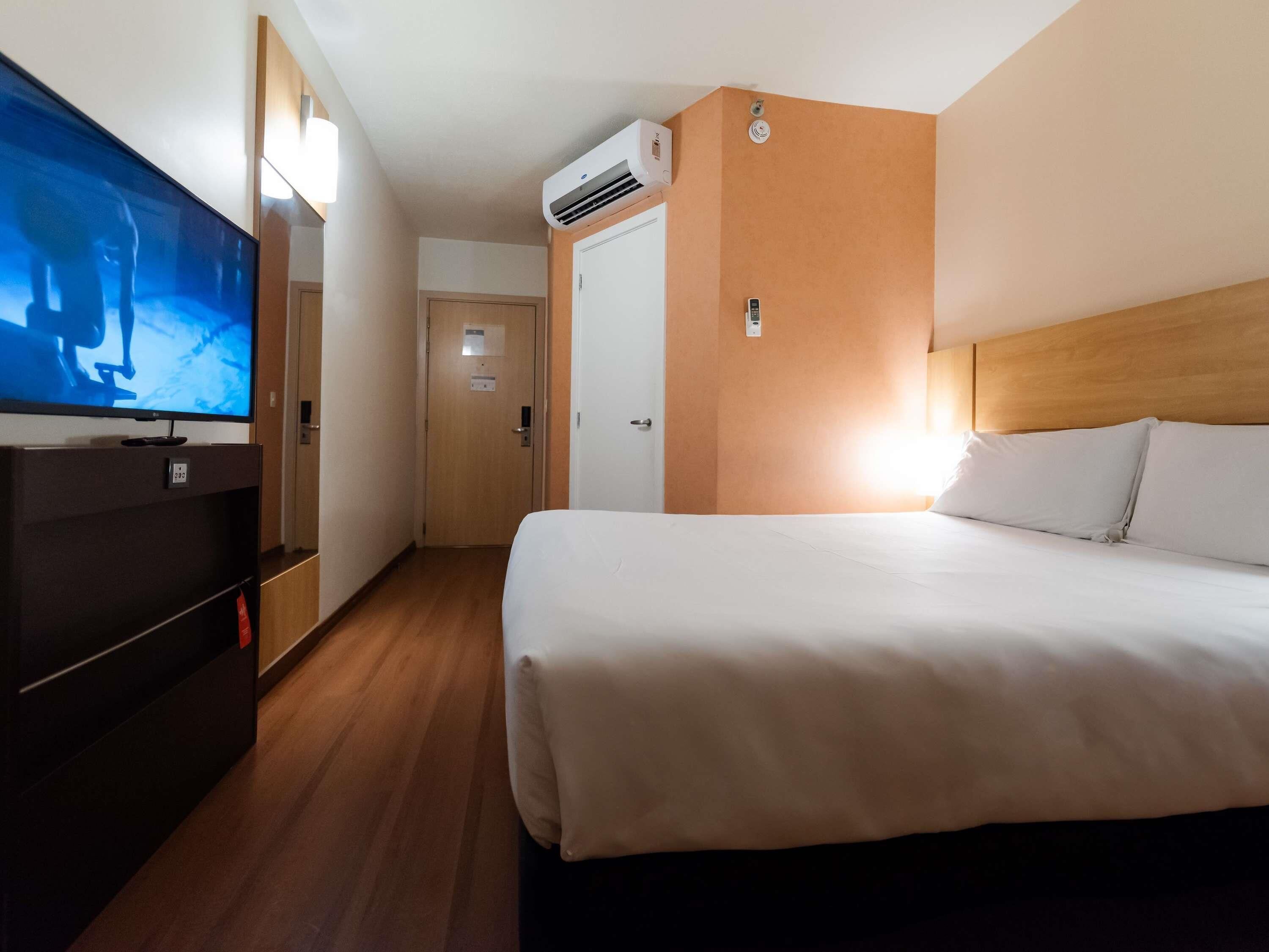Een hotelkamer met een bed, een televisie, een airconditioning en een houten hoofdeinde.