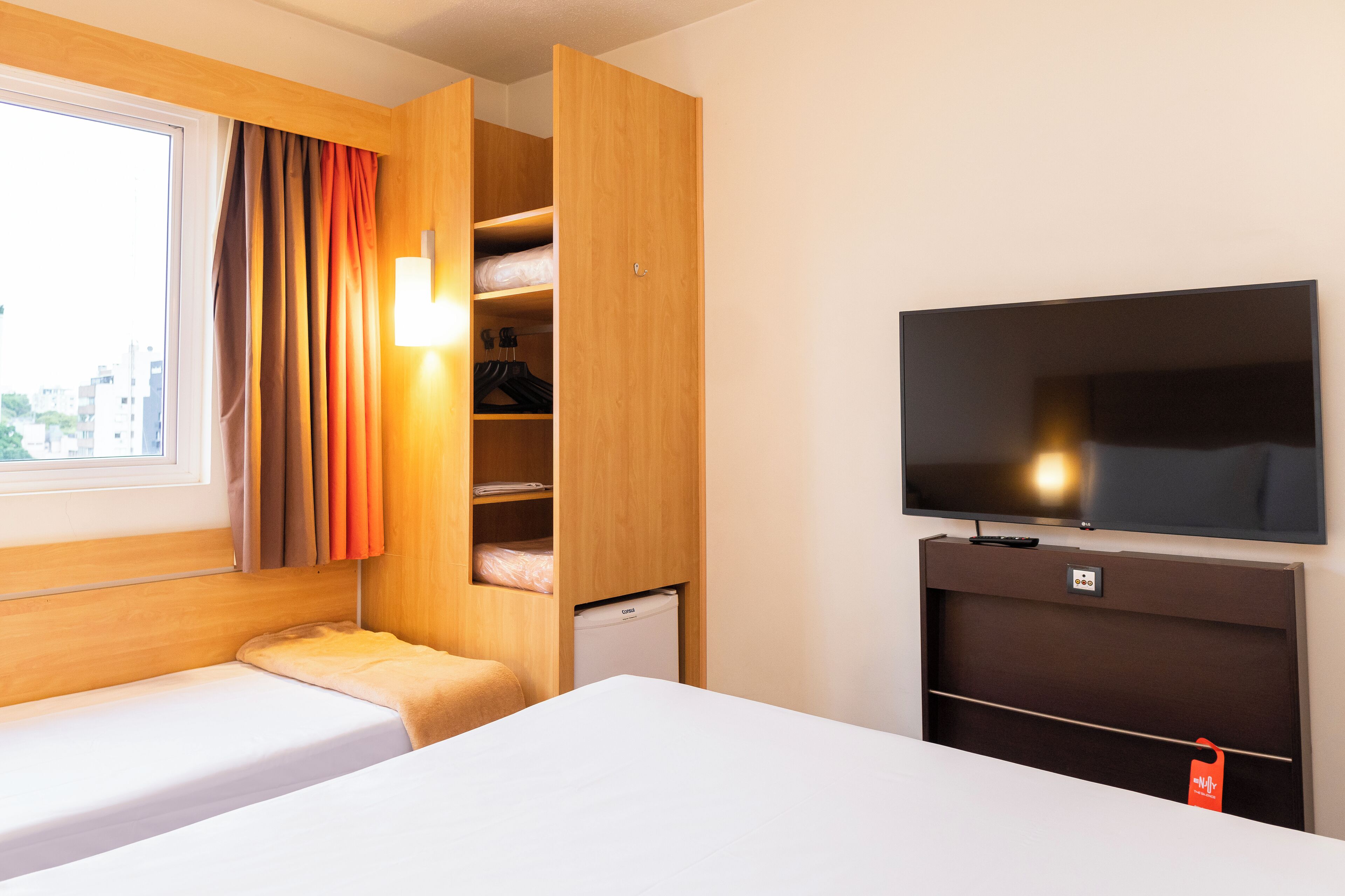 Habitación de hotel con cama, televisor, armario y ventana con cortinas.