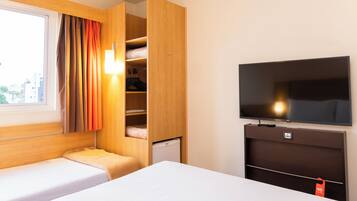 Habitación de hotel con cama, televisor, armario y ventana con cortinas.
